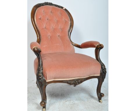A 19th century Victorian spoon back arm chair having a carved mahogany show wood frame, upholstered in pink fabric, button ba
