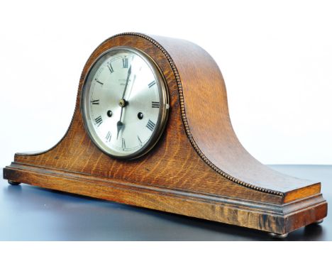 An early 20th century 1930's oak Napoleons hat mantel 8 day clock having a beading to the edge, silvered clock face, Roman nu