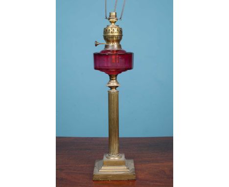 A Victorian oil lamp with brass column support beneath a cranberry glass reservoir, later converted for use an an electric ta