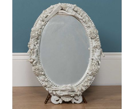 A Dresden porcelain framed oval mirror on an adjustable tripod stand, the frame topped with musical instruments and a torch, 