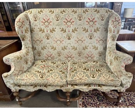 A Carolean style wing back sofa with floral upholstery and turned legs united by two X formed stretchers, 155cm wide