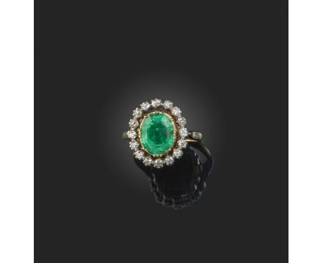 An emerald and diamond cluster ring, the oval emerald set within a surround of old cushion-shaped diamonds in silver and gold