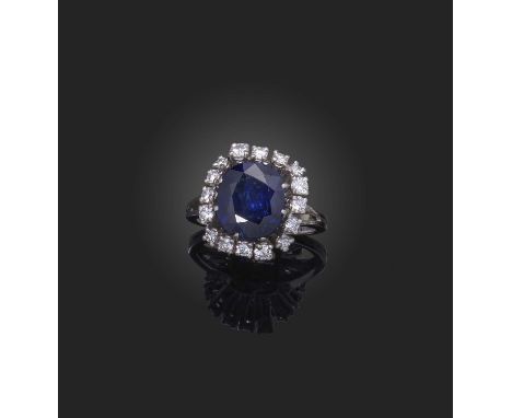 A sapphire and diamond ring, of cluster design, claw-set with a cushion-shaped sapphire weighing 4.78 carats, within a border