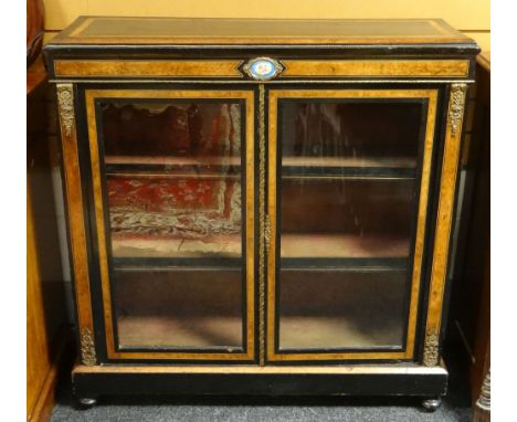 A two-door ebony and walnut bookcase, ormolu mounted and with oval floral painted porcelain tablet, circa 1890s, 105cms