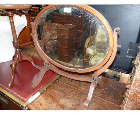 An oval Mahogany swing mirror having bevelled glass, frame requires a small repair/gluing, 24 1/2'' wide x 21'' high.