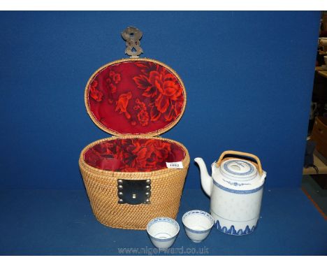 A wicker carrying basket with metal handles containing oriental Teapot and two cups.