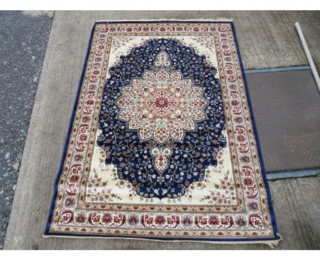A large border patterned and fringed rug with large central flower in cream with dark blue surround and beige and cream borde