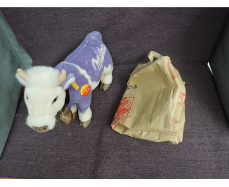 A modern Steiff Milka Lilac Cow having yellow tag 354014 and circular tag, wearing cow bell, with paper carry bag