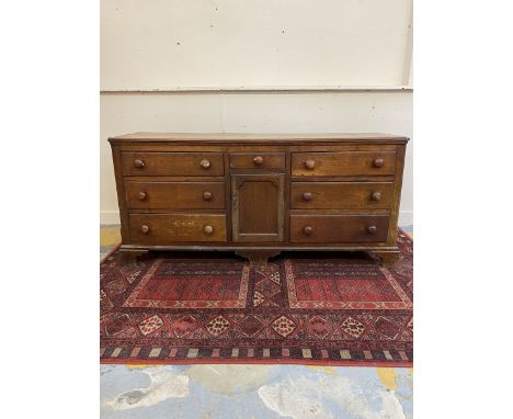 A George III oak dresser base of seven drawers, central cupboard and canted corners, raised upon bracket feet, 74 3/4" wide x