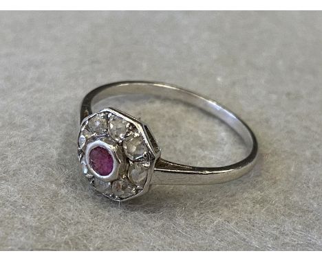 An Art Deco style white metal (probably gold) ring set with a central ruby surrounded by eight diamonds. 