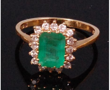 An 18ct gold emerald and diamond cluster ring, arranged as a centre claw set baguette cut emerald weighing approx. 1.5ct in a