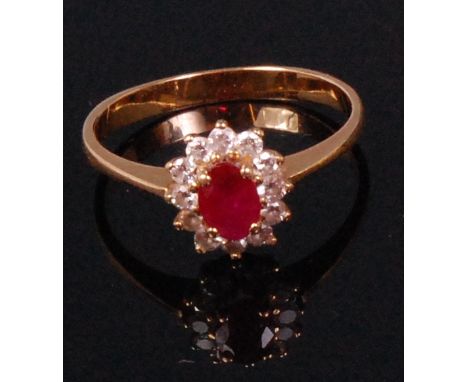 A ladies yellow metal ruby and diamond cluster ring, arranged as a centre four claw set oval cut ruby weighing approx 0.5ct, 