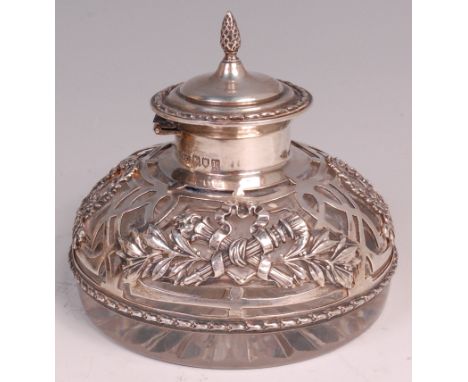 An Edwardian silver mounted glass inkwell, having a finial topped hinged dome cover, the silver worked as laurel wreaths, rib