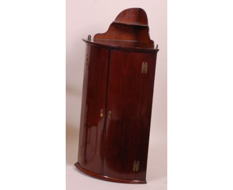 An early 19th century mahogany bowfront hanging corner cupboard, with galleried shelf over, the doors enclosing fitted shelve
