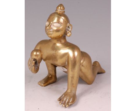 An Indian heavy brass deity figure of Balakrishna, in crawling pose with butter ball, with enamel porcelain set eyes, h.13cm 