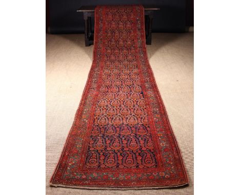 A Carpet Runner woven predominantly in claret, mid and dark blue wools with rows of repeated botehs in a triple banded border