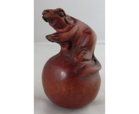 A carved wooden netsuke of a rat standing on a ball, 5.5cm high