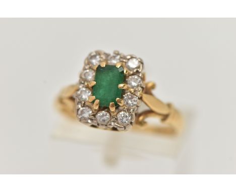 A YELLOW METAL EMERALD AND DIAMOND CLUSTER RING, of a rectangular form, set to the centre with an emerald cut emerald, raised