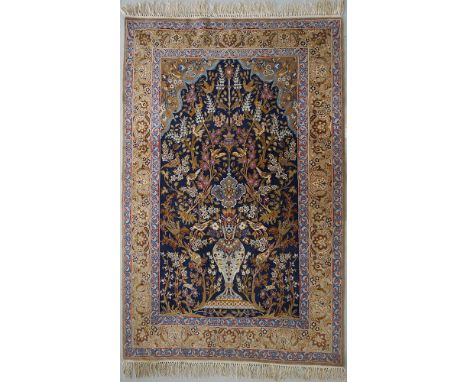 A very fine Persian / Iranian wool carpet with a vase, trees and birds decoration under an arch on a dark blue ground, surrou