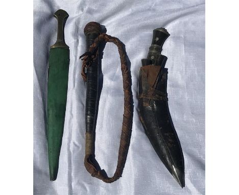 A plaited leather whip, A Gurkha knife in scabbard and a brass handled dagger in wood and green skin sheath.