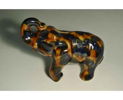 A Denby 'majolica' elephant money bank, standing with trunk raised, in mottled brown and cobalt blue, inscribed in gilt Geoff
