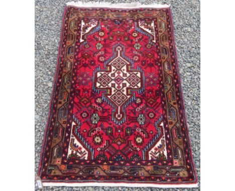 A Hamadan rug, north west Persia, the red field with an ivory lobed medallion, within a brown meandering vine border, 122 x 7