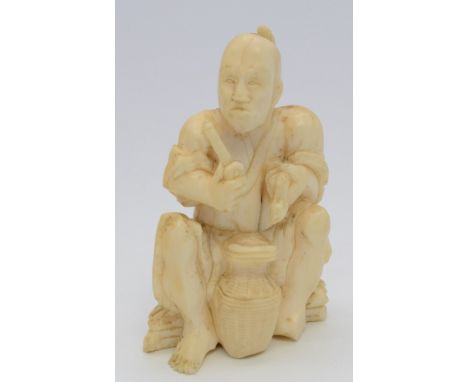 A Japanese ivory okimono, a man with Samurai hairstyle seated upon a tied bundle of wood while holding in his hands a snake a