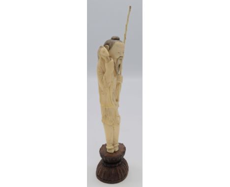 A Chinese ivory figure of a fisherman, holding a rod in one hand and carrying a fish over his shoulder, on a carved hardwood 