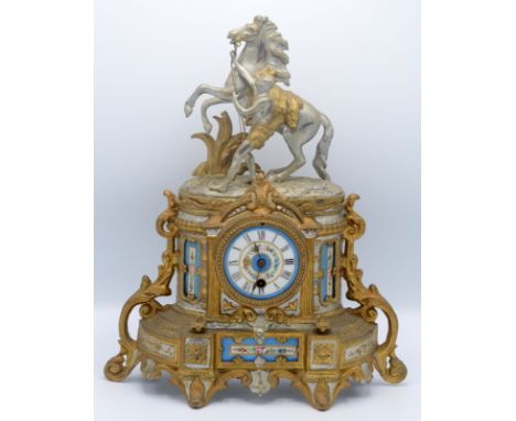 A 19th century gilt metal and spelter mantel clock, the circular painted enamel dial surmounted by a man with a rearing stall