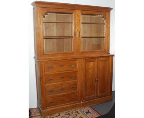 A continental light oak cabinet, the upper section with two glazed doors opening onto adjustable shelves, the base with a tie