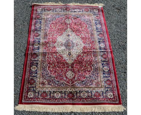 A rug, the red field with an ivory lobed medallion within a blue arabesque border, 171 x 117cm. 