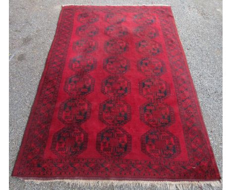 An Afghan carpet, the red field with seven rows of three large octagonal medallions, within a hooked gul and starburst motif 