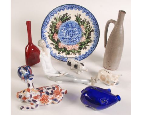 A Lladro figure of a seated man holding a book, incised number '23 D', length 27cm, five ceramic models of pigs, a red glass 