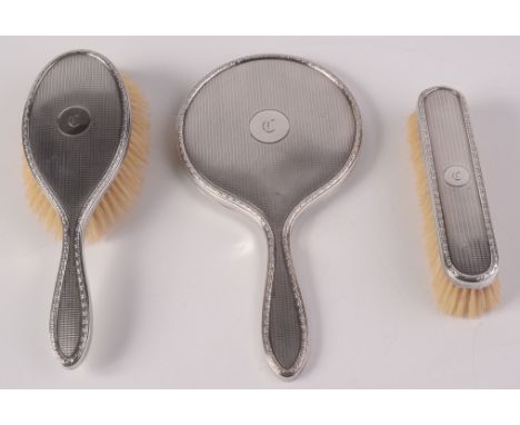 An engine turned, silver mounted hand mirror and two matching brushes. 