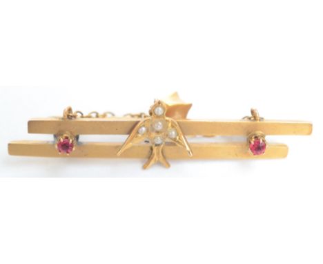 A 9ct gold bar brooch mounted with a pearl set swallow flanked by red stones.