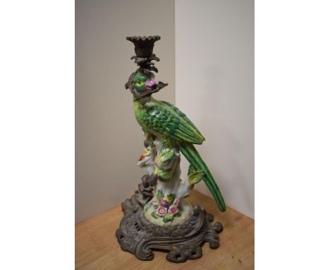 An attractive cast gilt metal and porcelain candlestick, formed as a perched parrot holding a sprig of foliage and surmountin