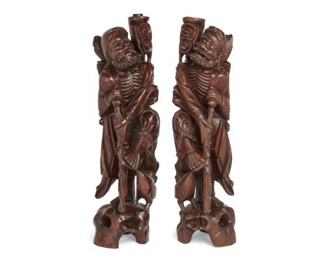 A pair of Chinese carved hardwood figural lamp bases,Early 20th century,Each carved as an emaciated man supported by a crutch