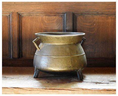 17th Century alloy cauldron with angular lug handles and medial band on truncated tripod supports, 33.5cm diameter x 23.5cm h