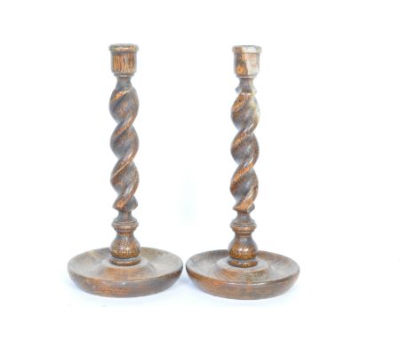 A pair of two oak barley twist candlestick holders with drip trays. Of typical form with a circular base. Measures approx. 30
