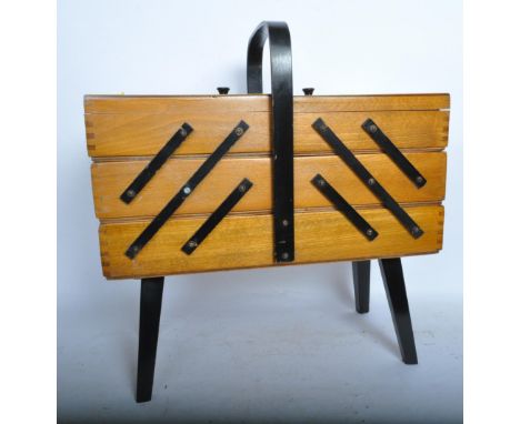 A retro vintage mid 20th century teak sewing box having cantilever shelves raised on ebonised supports and carry handle to th