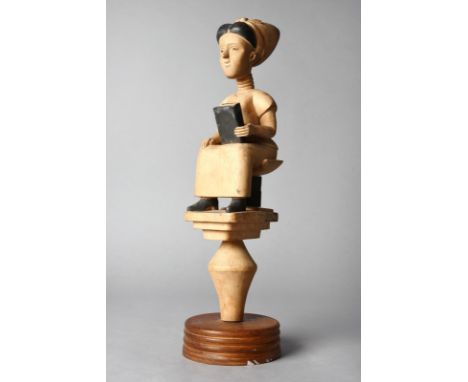 An Ashanti colon female figure Ghana wearing a ribbon tied bonnet and with a ringed neck, holding a book and seated on a book