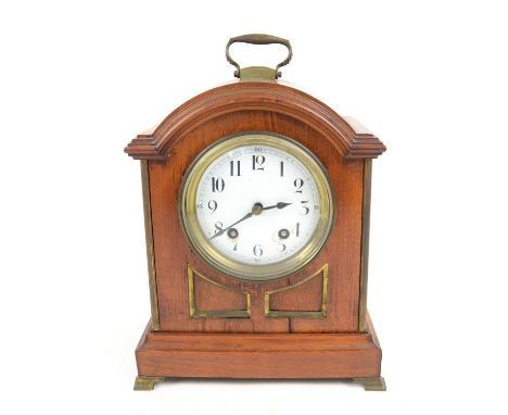 Edwardian walnut mantel clock with brass mounts, of arched form with swing handle and enamelled dial, the twin train movement