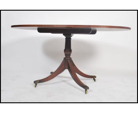 A Regency style walnut and mahogany oval breakfast / loo tilt top dining table. The crossbanded oval top raised on tilt mecha