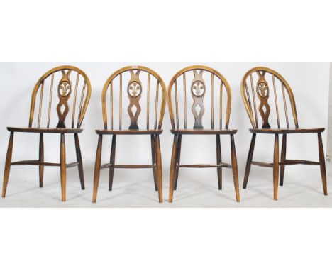 A set of 4 20th century Ercol beech and elm wood ' fleur de lys ' dining chairs being raised on turned legs with saddle seats