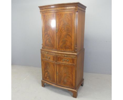 A modern cross-banded flame mahogany veneered drinks cabinet, with four doors, two drawers, pull-out slide and raised on brac