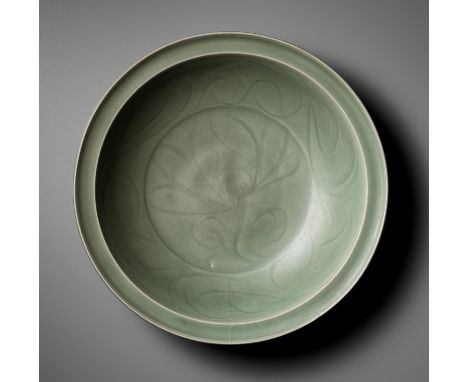 A CARVED LONGQUAN CELADON 'LOTUS' CHARGER, MING DYNASTY 明代龍泉青釉暗刻蓮紋折沿盤China, 1368-1644. The deep rounded sides supported on a 