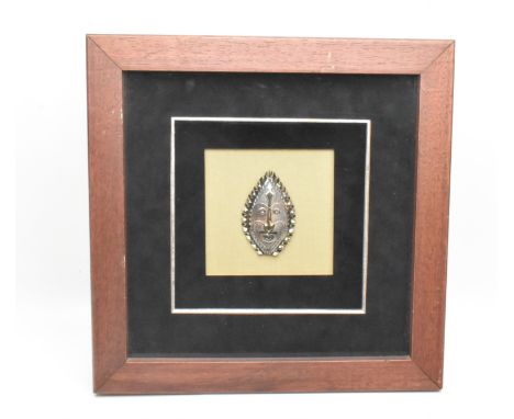 A framed white metal and enamel tribal mask The mask having enamel detailing and etched detailing. The tribal art typical of 