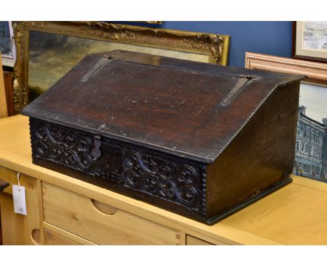 A late 17th century oak bible box, the slope front with iron strap hinge and lock plate over a floral carved front panel, all