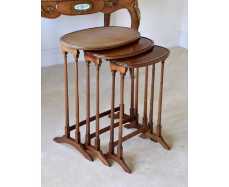 An Edwardian nest of three oval mahogany tables, the satinwood banded tops raised on slender ring turned supports with arched