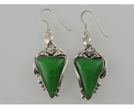 A pair of white metal and jade ear pendants, the triangular stones within a naturalist frame and suspended from a leaf-shaped